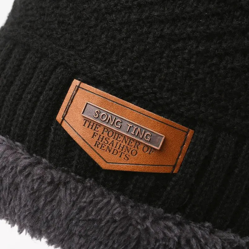 Close-up of a black knit beanie with a brown leather label featuring text.